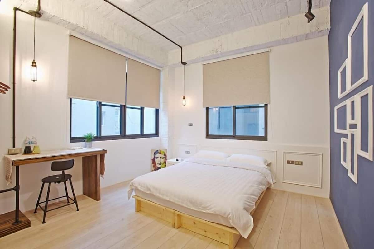 Un dormitorio con cama, escritorio y silla, y ventanas amplias.