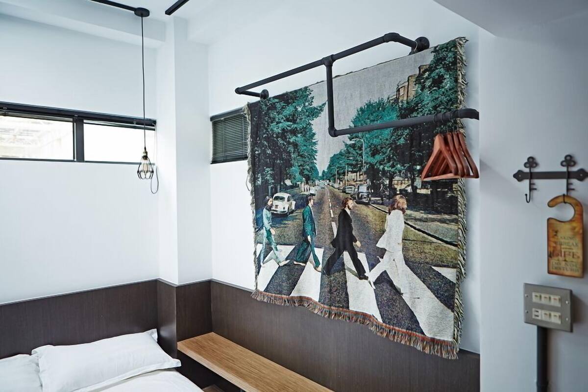 Un dormitorio con un gran mural en la pared que muestra un cruce de cebra, una cama, un banco y una lámpara colgante.