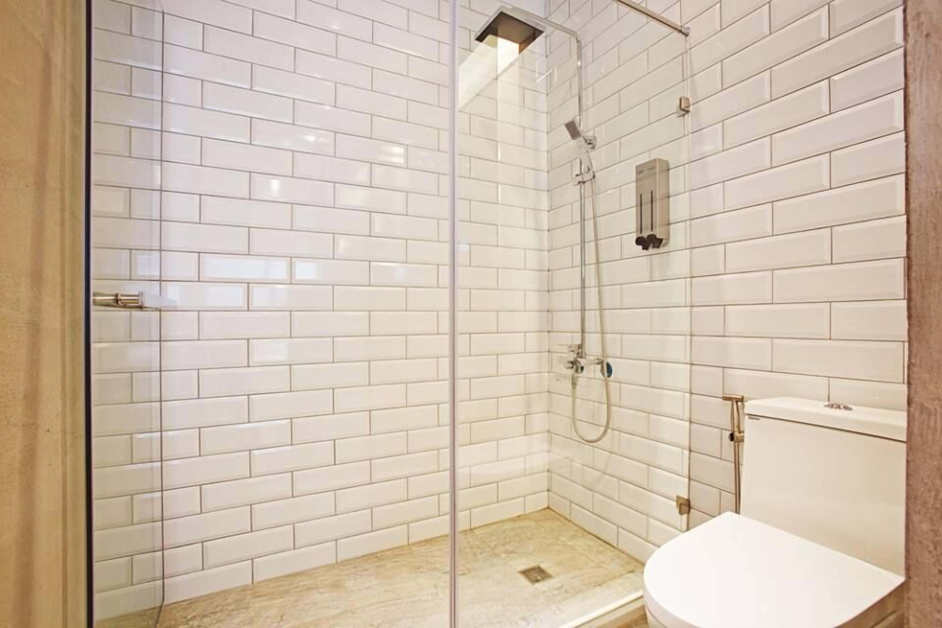 A modern bathroom with white subway tiles, a glass-enclosed shower, and a white toilet.