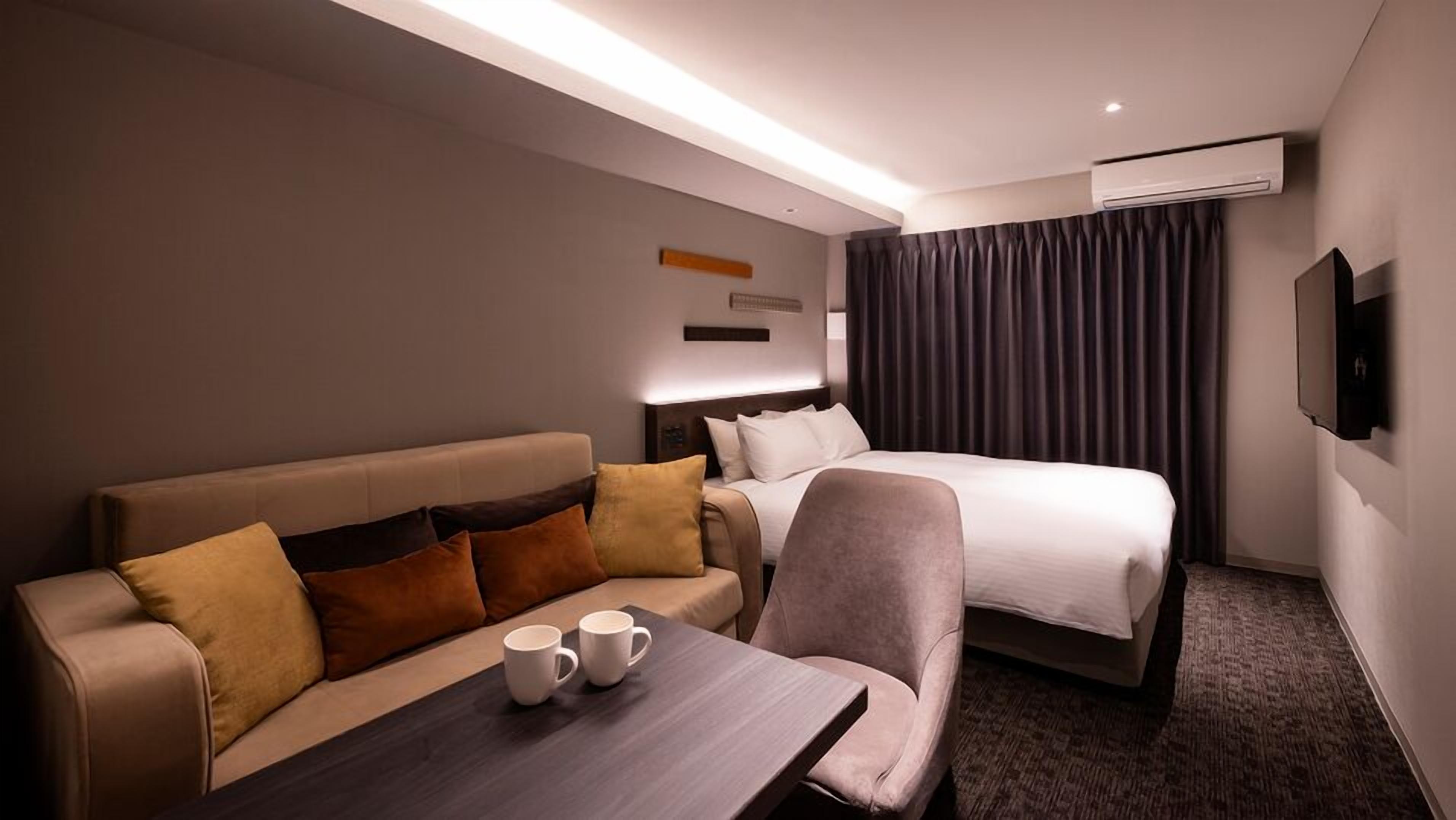 Habitació d'hotel amb un llit, un sofà, una taula amb una tassa de cafè i un aparell d'aire condicionat.
