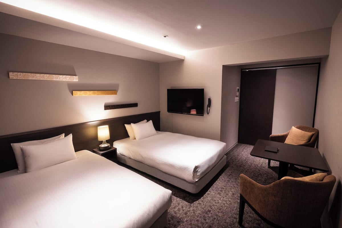 Une chambre d’hôtel avec deux lits, un bureau, une chaise, une télévision et une porte.