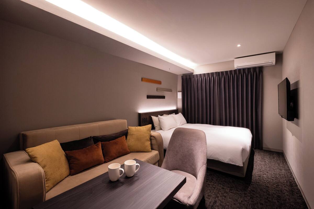 Une chambre d’hôtel avec un lit, un canapé, une table avec deux tasses et un appareil de climatisation.