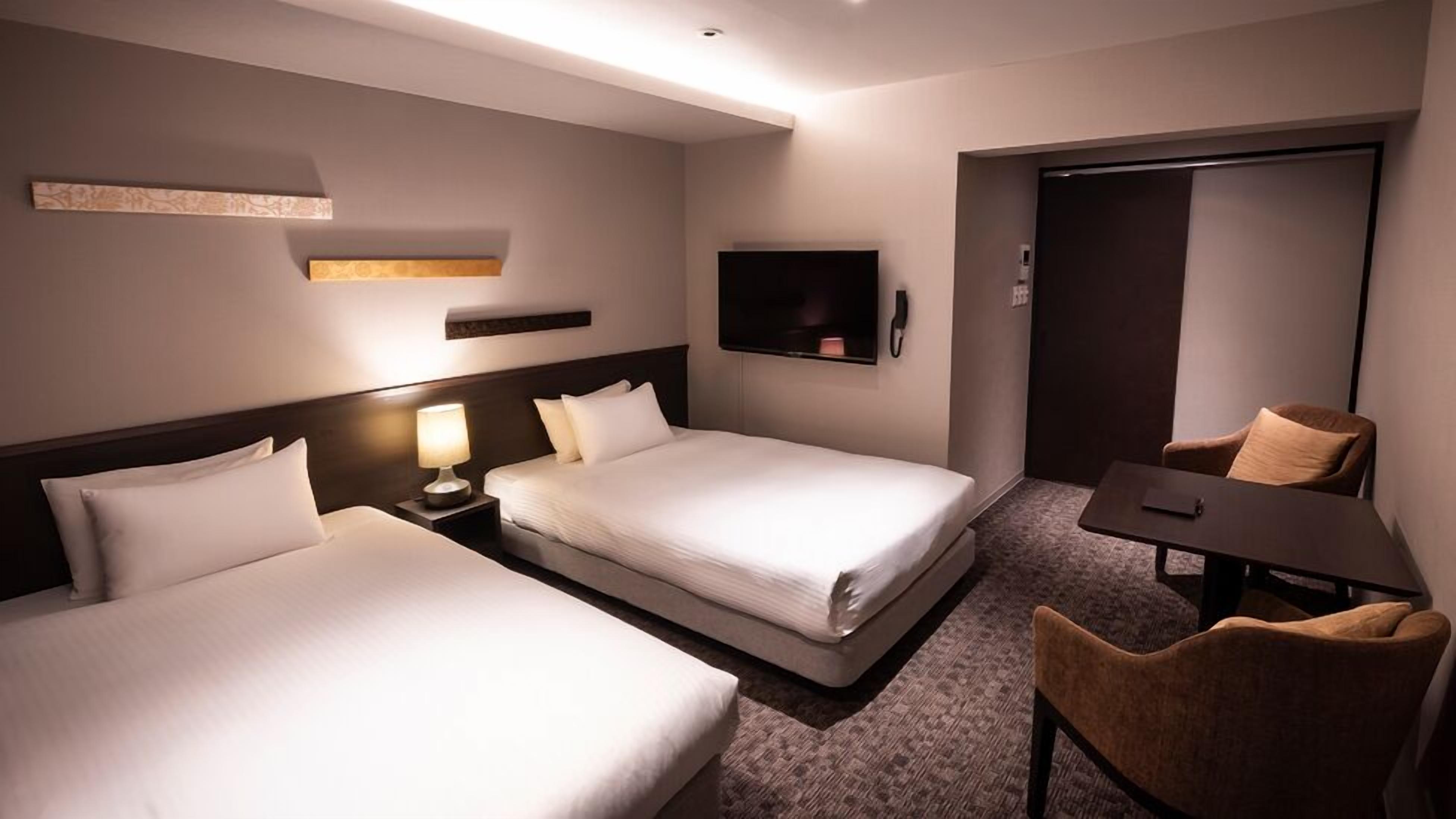 Una habitació d'hotel amb dos llits, una taula de treball, una cadira, un televisor i un armari.