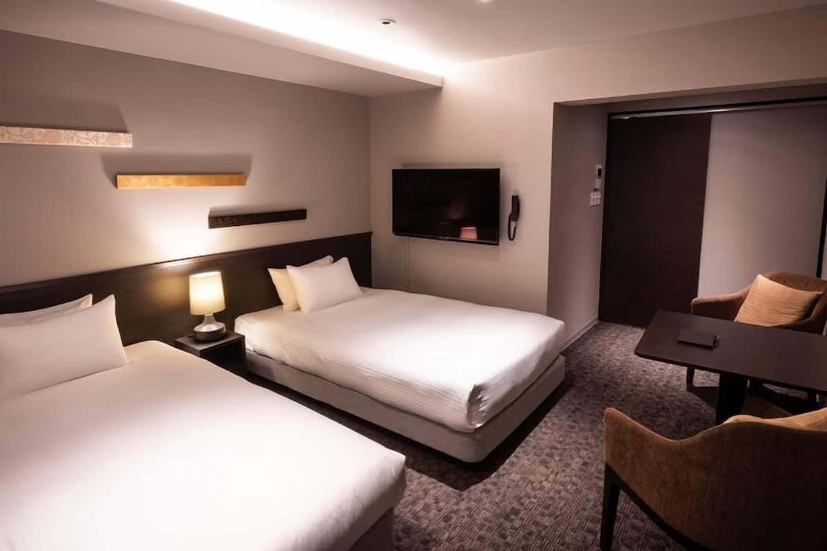 A hotel room with two beds, a desk, a chair, a TV, and a wardrobe.