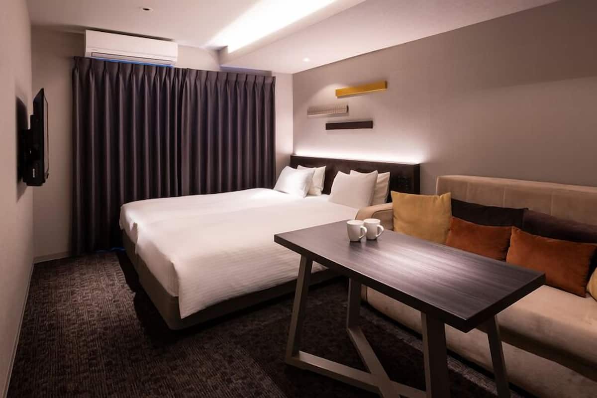 A hotel room with a bed, a sofa, a coffee table, and a flat-screen TV.