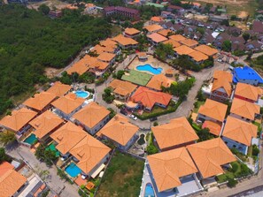 An aerial view of a residential area with uniform orange-roofed houses, a central swimming pool, and a small park. - Garden Villa - Pattaya Holiday House Walking Street (Pattaya)