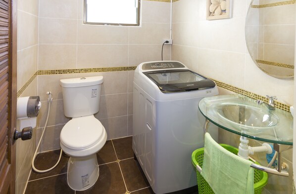 A compact bathroom with a toilet, washing machine, and glass sink.