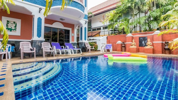 Una piscina con sillas de descanso y juguetes inflables, rodeada por un edificio de fachada roja y blanca y un balcón.