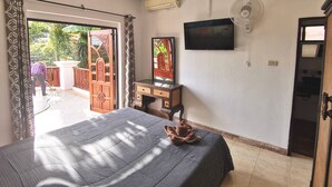 Un dormitorio con cama, televisor, ventilador y puerta que da a un balcón.