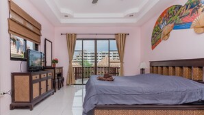 Un dormitorio con cama, televisión sobre un mueble, ventana con cortinas y balcón con vistas a edificios.