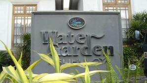 Une enseigne indiquant « Jardin aquatique », avec un logo au-dessus, le tout entouré de verdure.