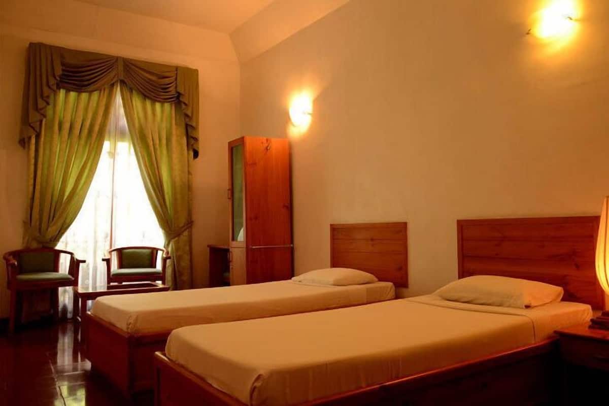 Une chambre avec deux lits simples, une armoire en bois, un bureau, une chaise et une lampe.