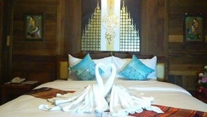 Een houten kamer met een bed, twee kussens, een wand met een decoratief paneel en een kleine tafel met een telefoon.