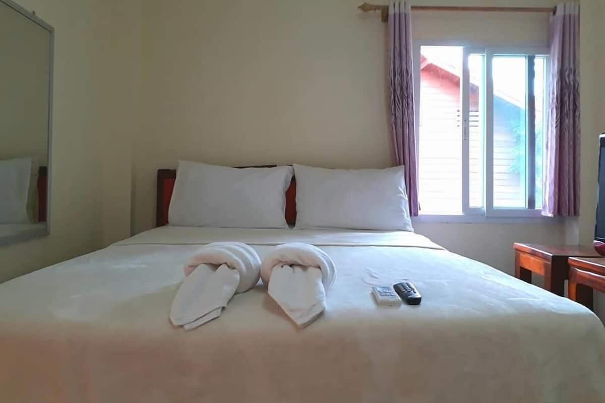 Un lit bien fait, avec des draps blancs, une télécommande et des serviettes posées sur le lit.