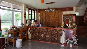 Een receptie met een houten, houtgesneden balie, een klok en diverse decoratieve objecten.