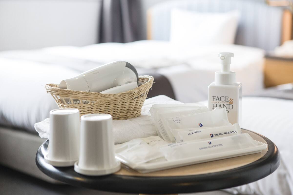 A tray with toiletries including a facial cleanser, a hand soap dispenser, and a razor on a bed.