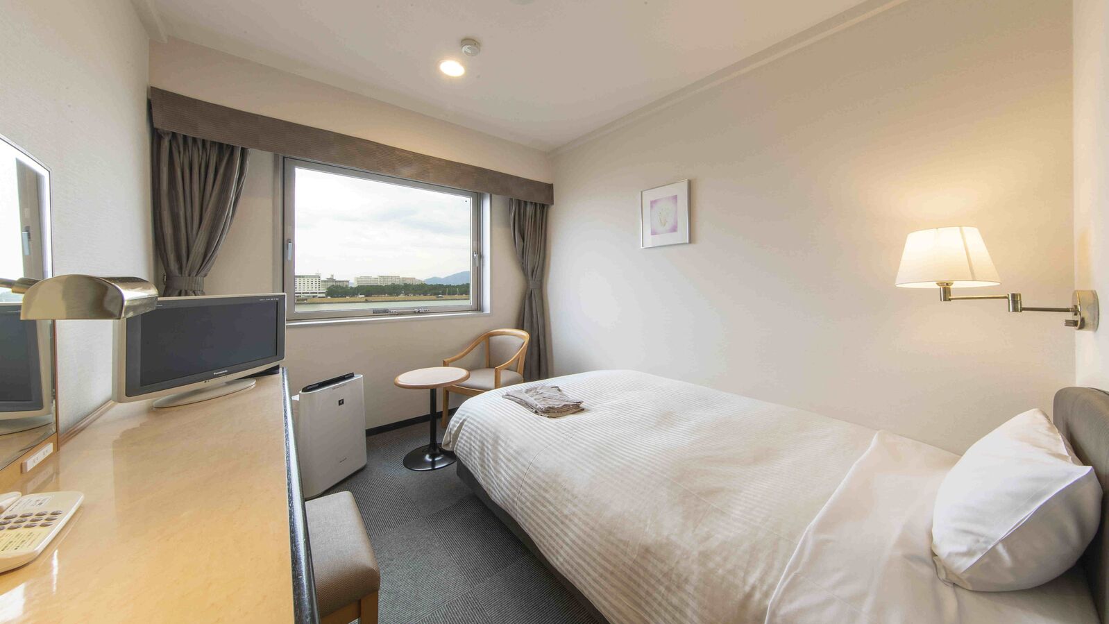 Ein Hotelzimmer mit einem Bett, einem Schreibtisch mit Computer, einem Sessel, einem kleinen Tisch und einem Fenster mit Vorhängen.