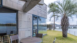 An outdoor seating area with a table and chairs, a palm tree, and a view of a river and bridge. - Karatsu Daiichi Hotel Riviere (Karatsu)