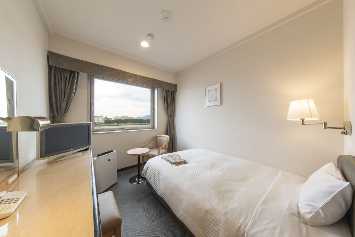 A hotel room with a bed, desk, chair, and a window with curtains.