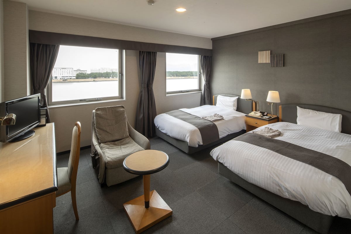 A hotel room with two beds, a desk, a chair, and a small table.