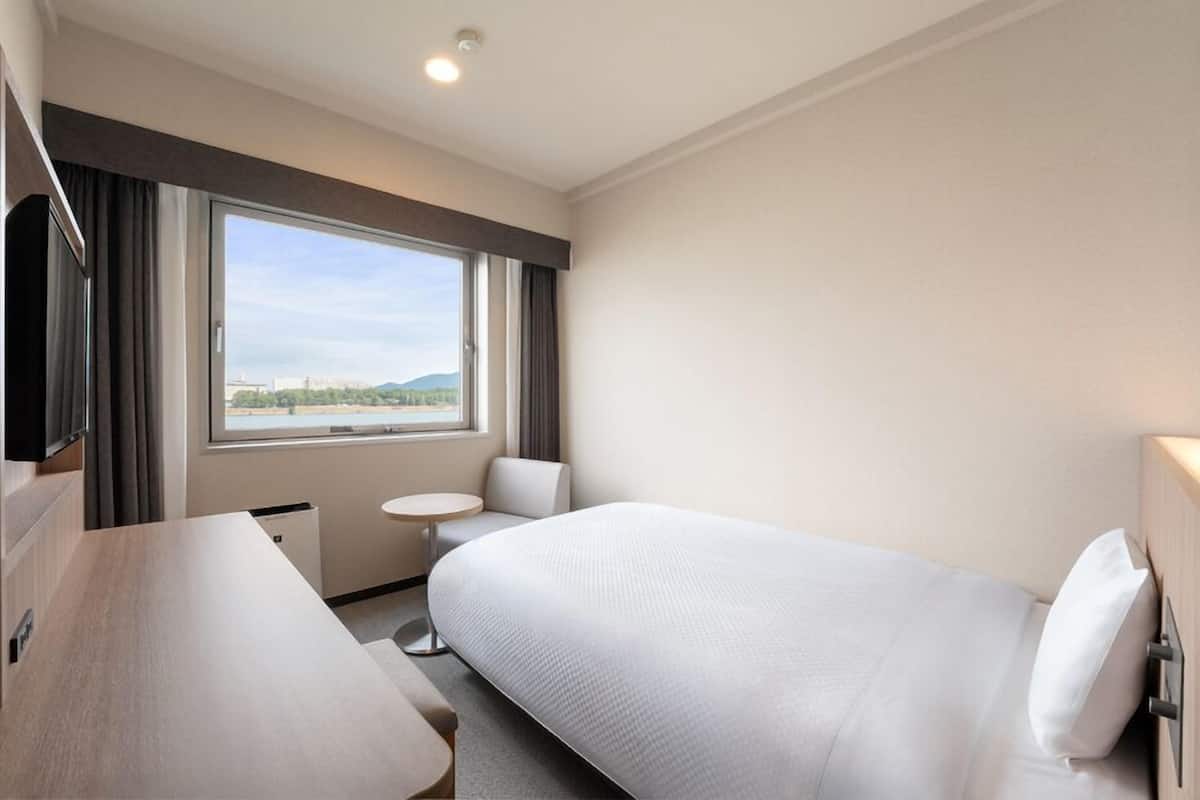 A hotel room with a bed, a desk, a chair, a small table, and a window with a view.