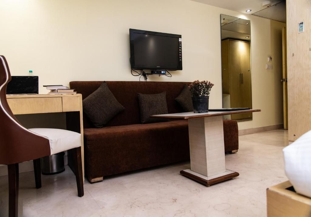 A hotel room with a sofa, a desk with a laptop, a television, and a small table with a plant.