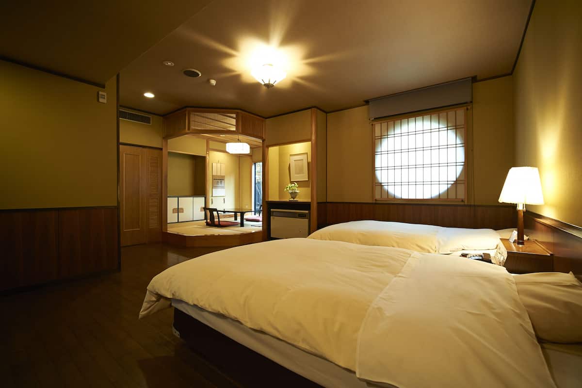Une chambre d’hôtel avec deux lits, un bureau, une chaise, une fenêtre donnant sur un paysage agréable et un luminaire au plafond.