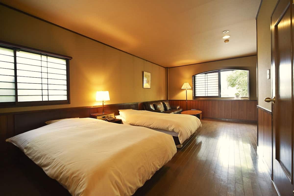Une chambre d’hôtel avec deux lits, un canapé, une petite table et une fenêtre avec des stores.