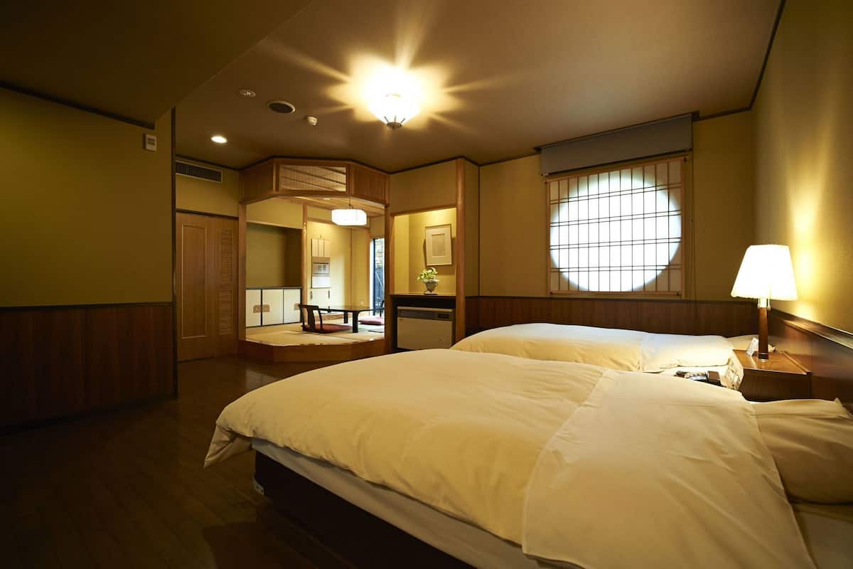 Une chambre d’hôtel avec un grand lit, une table de chevet avec une lampe, une fenêtre donnant sur un beau paysage et un petit coin salon avec une table et des chaises.