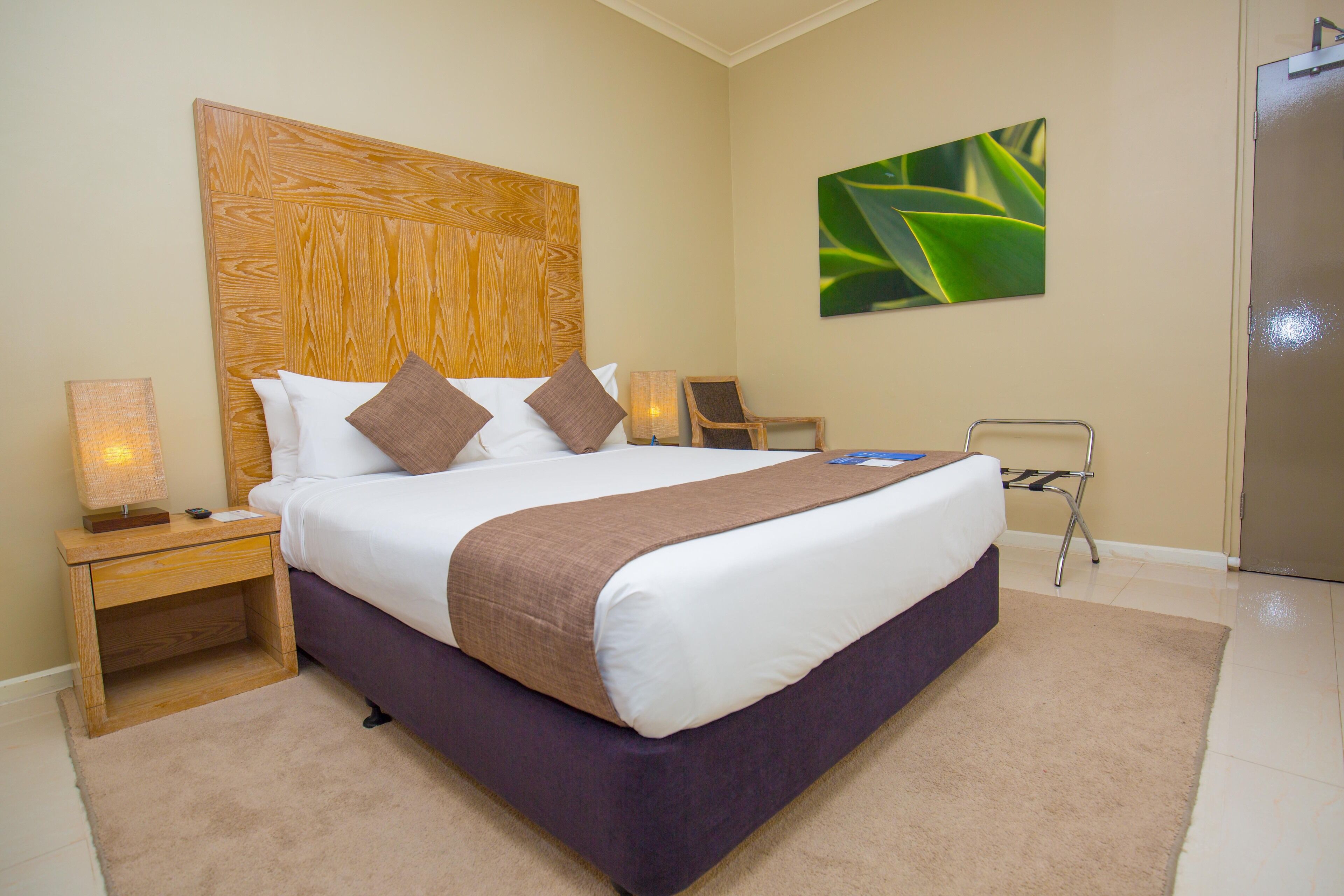 A neatly made bed with a wooden headboard, a bedside table with a lamp, and a chair.