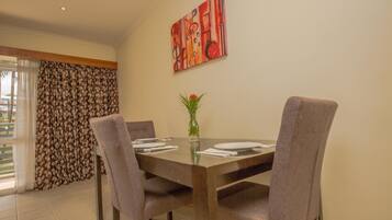 A dining area with a table set for four, a vase with flowers, and a painting on the wall.