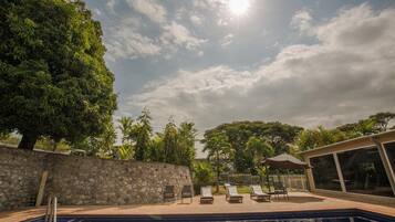 A swimming pool with lounge chairs, a stone wall, and a glass-enclosed building.