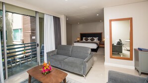 A modern hotel room with a grey sofa, a wooden coffee table with flowers, a bed with a grey headboard, and a large mirror on the wall. - Gateway Hotel (Port Moresby)