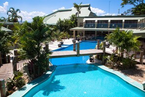A large outdoor swimming pool with multiple lanes, surrounded by palm trees and a building with a green roof. - Gateway Hotel (Port Moresby)