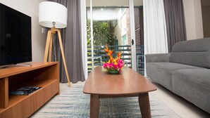 A modern living room with a flat-screen TV, a wooden coffee table with a floral centerpiece, a grey sofa, and a floor lamp. - Gateway Hotel (Port Moresby)
