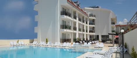 A modern hotel with a large pool, multiple balconies, and outdoor seating areas.