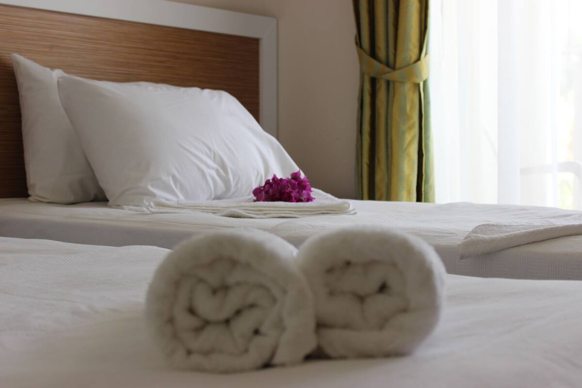 A neatly made bed with white linens, pillows, and rolled towels.