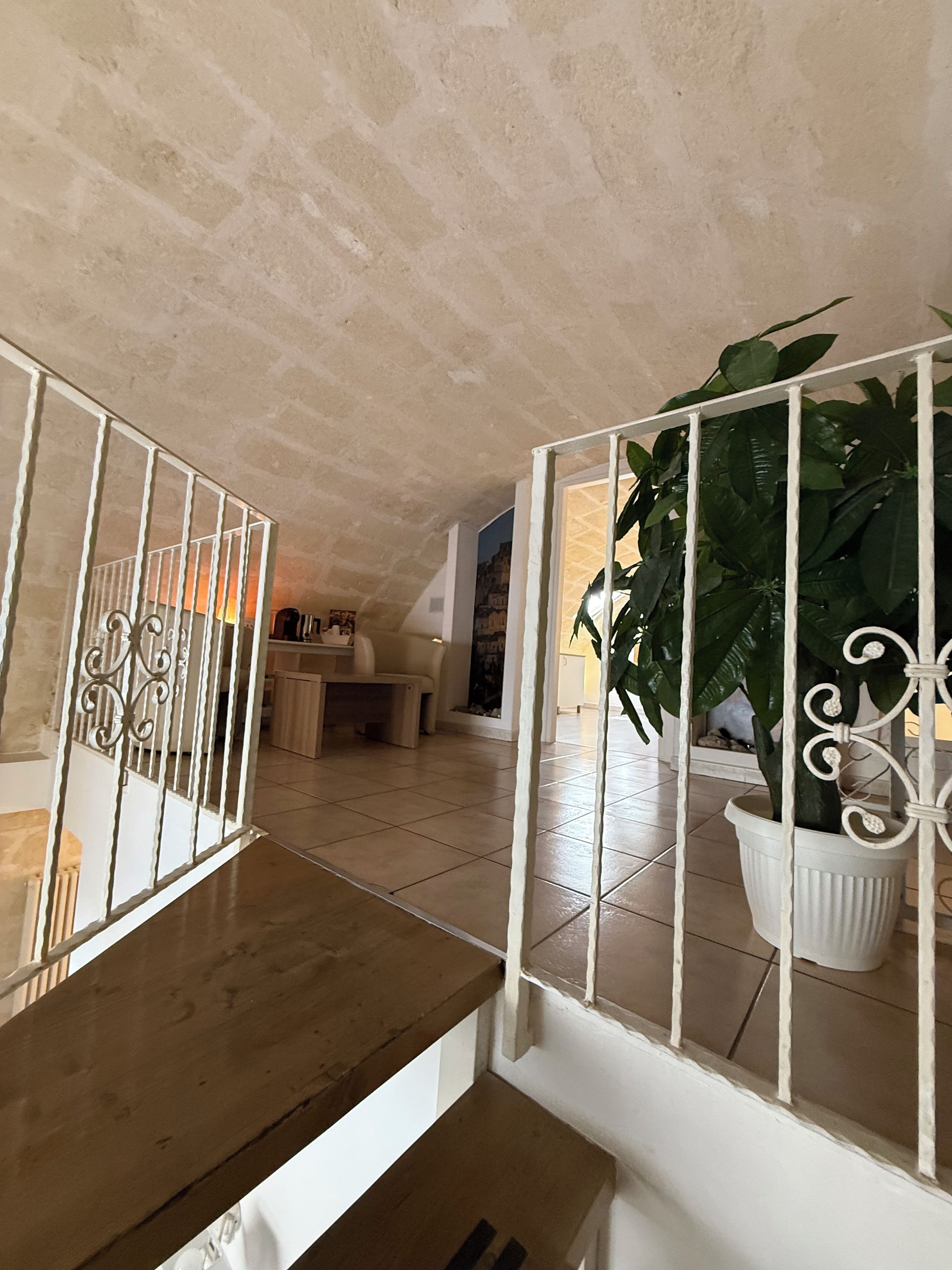 A spacious room with a tiled floor, a wooden bench, a potted plant, and a white railing.