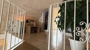 Una habitación amplia con suelo de baldosas, un banco de madera, una planta en maceta y una barandilla blanca.