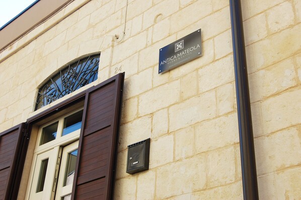 A building with a stone facade, a window with decorative ironwork, and a sign for "ANTICA MATEOLA ROOMS & SQUATS."