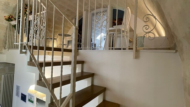 A staircase with white railings and wooden steps leading to a landing with a white chair and a table. - Antica Mateola Rooms&Suites (Matera)