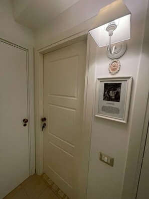 Un couloir avec une porte blanche, un luminaire fixé au mur et un tableau encadré avec du texte.