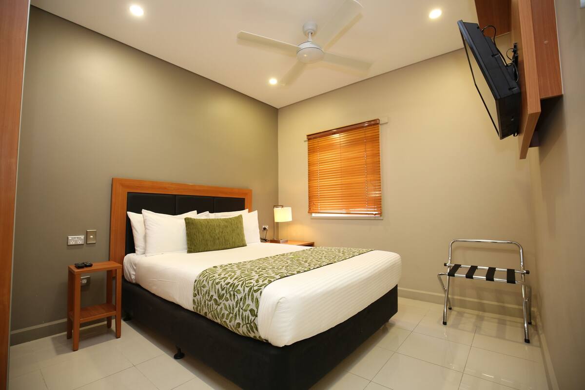 A neatly arranged bedroom with a bed, bedside table, lamp, and a TV mounted on the wall.
