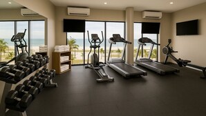 Un gimnasio con cintas de correr, mancuernas y un banco para pesas, con vistas a una playa.