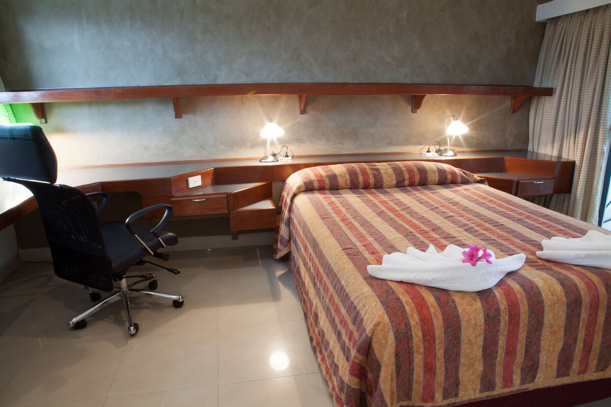 Camera d'albergo con un letto, una scrivania, una sedia e due lampade da comodino.