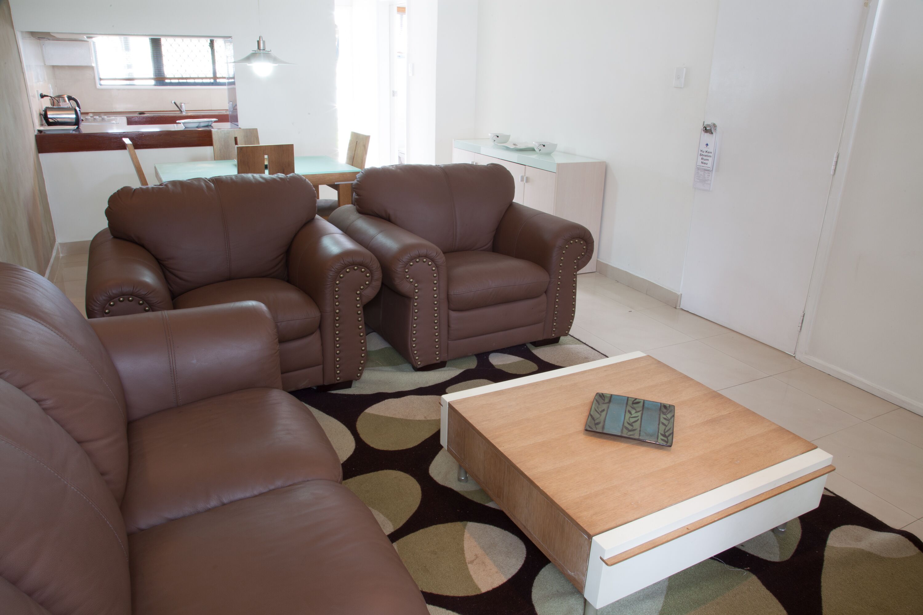 A living room with a brown leather sofa set, a wooden coffee table, and a patterned rug.