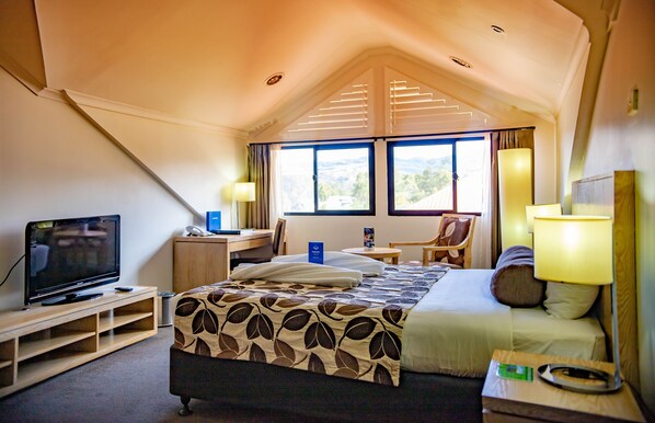 A hotel room with a bed, a desk, a television, and a window with a view of the outdoors.
