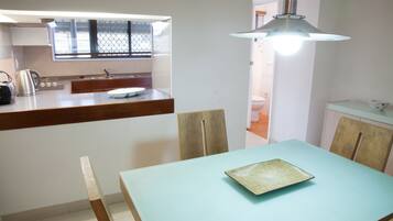 Un espace repas comprenant une table, des chaises, un luminaire, ainsi qu’un coin cuisine avec une fenêtre et un comptoir.