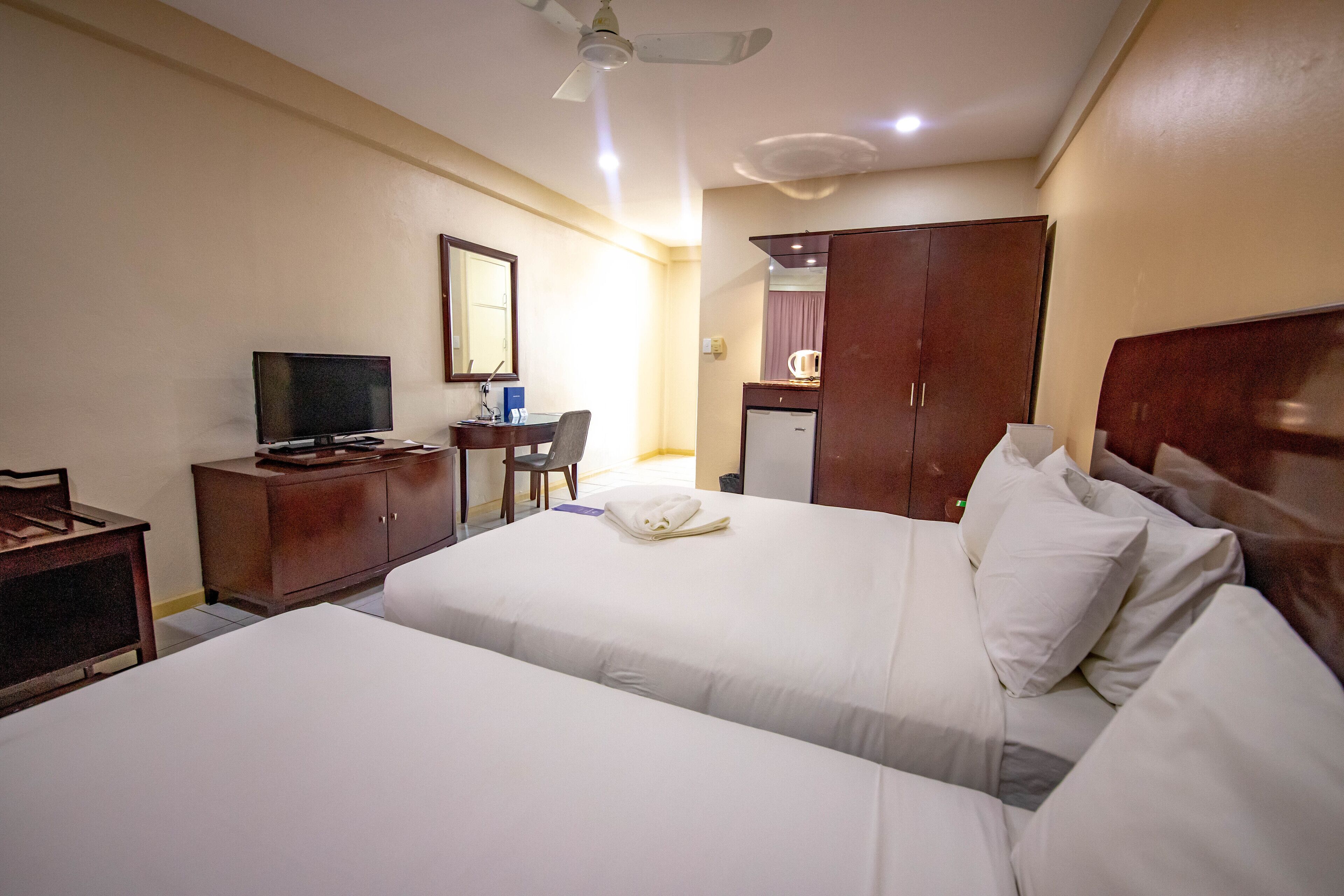 Habitación de hotel con dos camas, un escritorio con televisor, un armario y un espejo.
