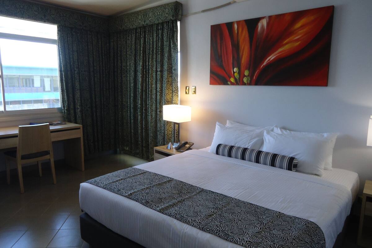 Une chambre d’hôtel avec un lit, un bureau, une chaise, une lampe et un tableau au mur.